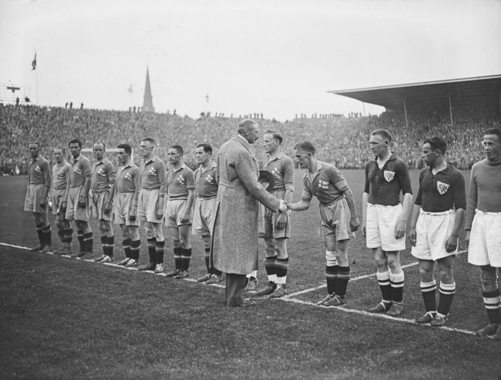 King Christian X of Denmark shaking hands with national team players on the pitch before an international football match.
